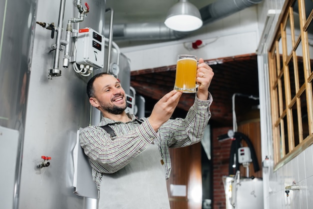 Un giovane birraio barbuto conduce il controllo di qualità della birra appena prodotta nel birrificio.