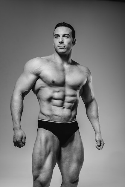 Un giovane bodybuilder atleta posa in studio in topless, mostrando i suoi addominali e muscoli. Bianco e nero.