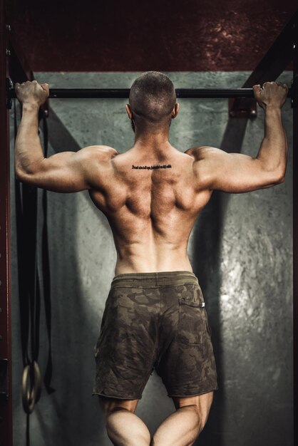 Un giovane bodybuilder muscoloso che fa esercizi di pull-up in palestra.