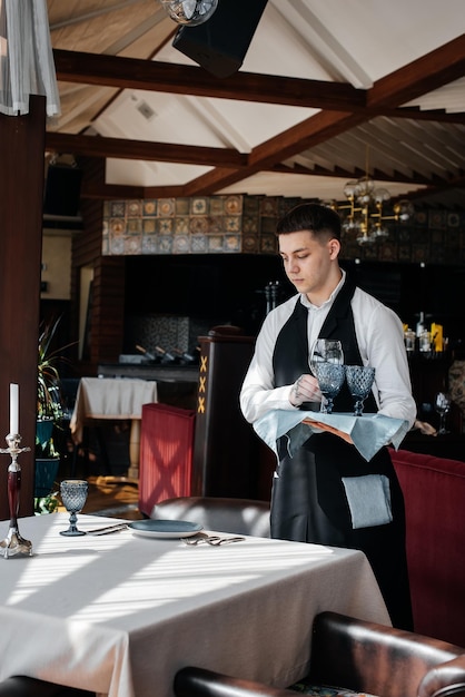 Un giovane cameriere in elegante uniforme è impegnato a servire la tavola in un bellissimo ristorante gourmet Un ristorante di alto livello Servizio al tavolo nel ristorante