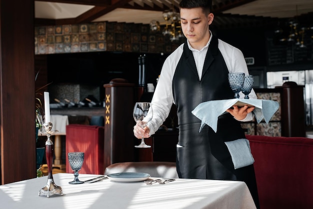 Un giovane cameriere in elegante uniforme è impegnato a servire la tavola in un bellissimo ristorante gourmet Un ristorante di alto livello Servizio al tavolo nel ristorante