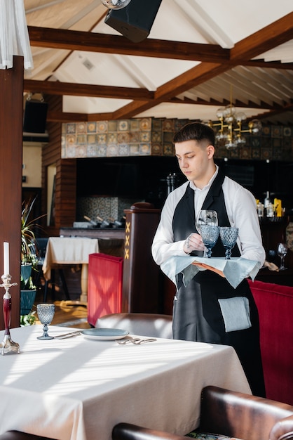 Un giovane cameriere in un'elegante uniforme è impegnato a servire la tavola in un bellissimo ristorante gourmet. Attività di ristorazione, di altissimo livello.