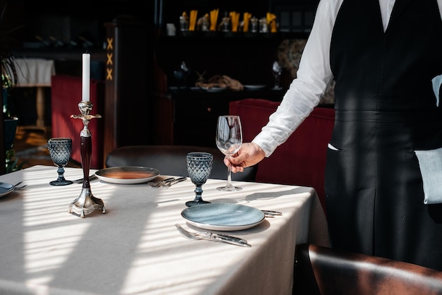 Un giovane cameriere in un'elegante uniforme è impegnato a servire la tavola in un bellissimo ristorante gourmet primo piano Servizio al tavolo nel ristorante