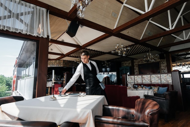 Un giovane cameriere in uniforme elegante è impegnato a servire la tavola in un bellissimo ristorante gourmet Un ristorante di alto livello Servizio al tavolo nel ristorante