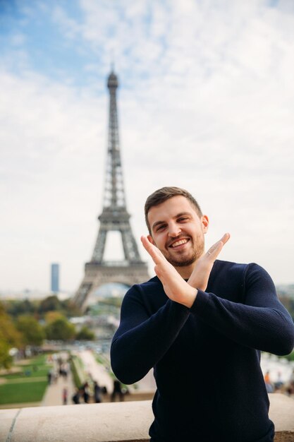 Un giovane che indossa una giacca blu scuro è in piedi sullo sfondo della Torre Eiffel Il tempo soleggiato è autunno