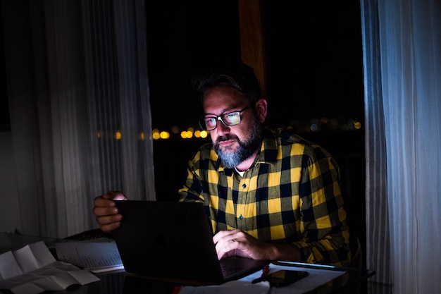 Un giovane che usa il laptop e lavora a un computer di notte a casa. Uomo d'affari al lavoro nel suo ufficio