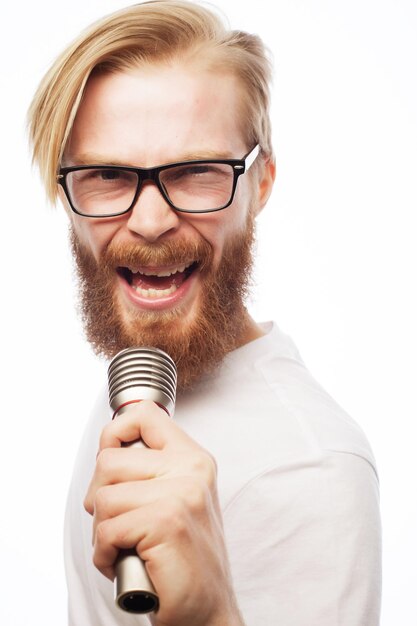 Un giovane con la barba che indossa una maglietta con in mano un microfono e canta, stile hipster. Su sfondo bianco.