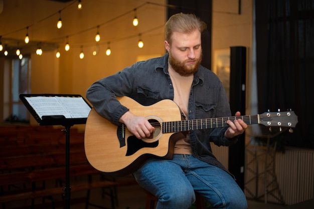 Un giovane con la barba suona una chitarra acustica in una stanza con luci calde