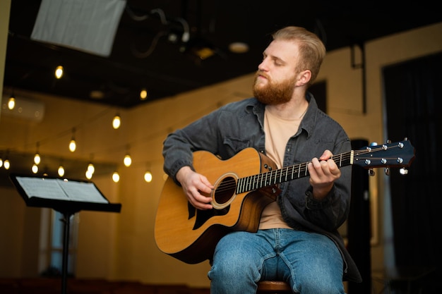 Un giovane con la barba suona una chitarra acustica in una stanza con luci calde