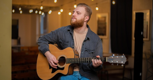 Un giovane con la barba suona una chitarra acustica in una stanza con luci calde