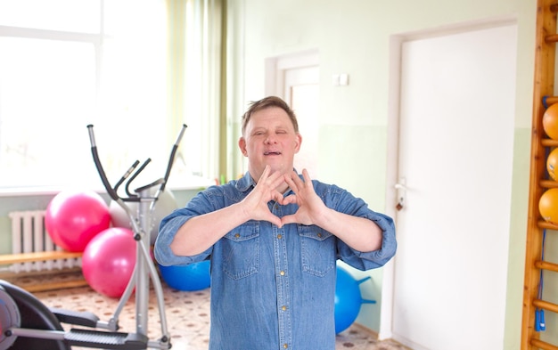 Un giovane con sindrome di Down vestito con una giacca di jeans casual sorridente a forma di simbolo del cuore con il concetto romantico delle mani