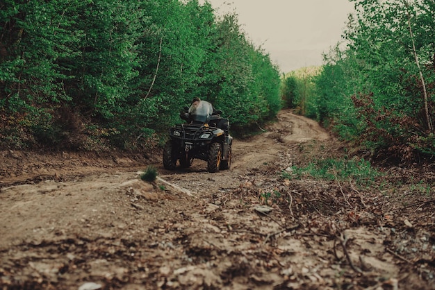 Un giovane con un casco bianco cavalca attraverso i boschi su un quad hobby estremo Un viaggio in quad sulla strada dai tronchi Quad bike attraverso la foresta