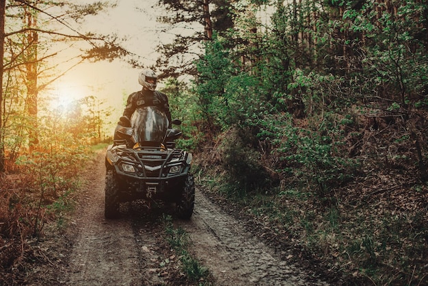 Un giovane con un casco bianco cavalca attraverso i boschi su un quad hobby estremo Un viaggio in quad sulla strada dai tronchi Quad bike attraverso la foresta