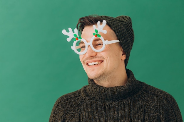 Un giovane con un maglione caldo, un berretto e occhiali da carnevale isolati su uno sfondo verde