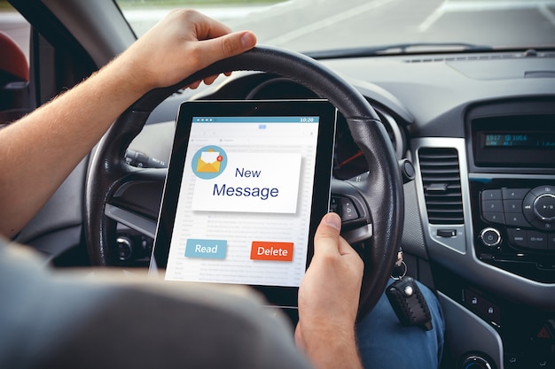 Un giovane con un tablet in mano al volante dell'auto.