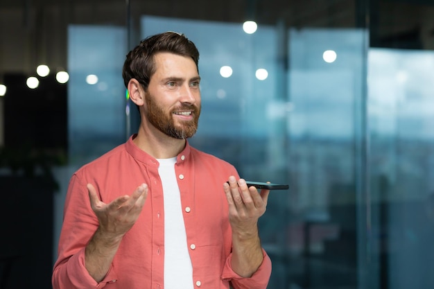 Un giovane con una camicia rossa siede in ufficio e parla al telefono attraverso i dischi dell'altoparlante