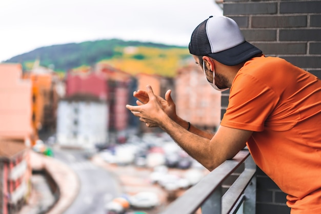 Un giovane con una maschera che applaude sul balcone alle 8 del pomeriggio. Coronavirus pandemico in Spagna