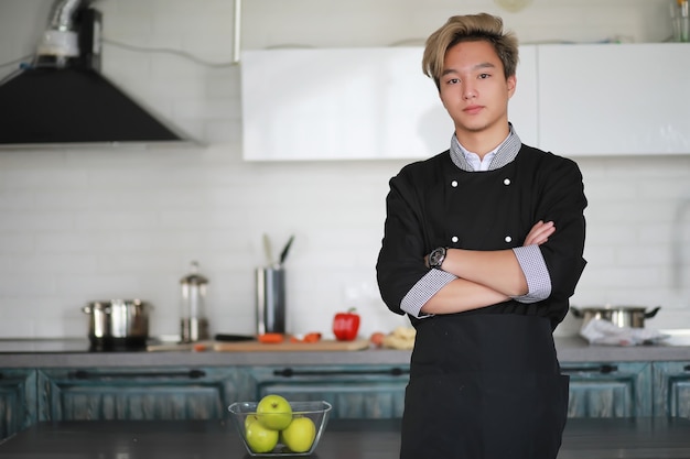 Un giovane cuoco asiatico in cucina prepara il cibo in un vestito da cuoco