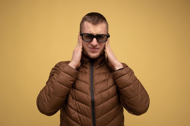 Un giovane degli anni '20 con una giacca marrone su sfondo giallo triste con gli occhiali per guardare un film in 3d si copre le orecchie con le mani da un suono forte