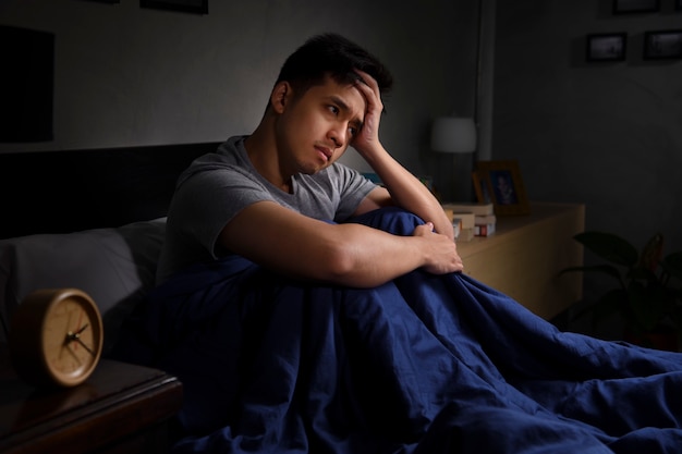 Un giovane depresso che soffre di insonnia seduto a letto