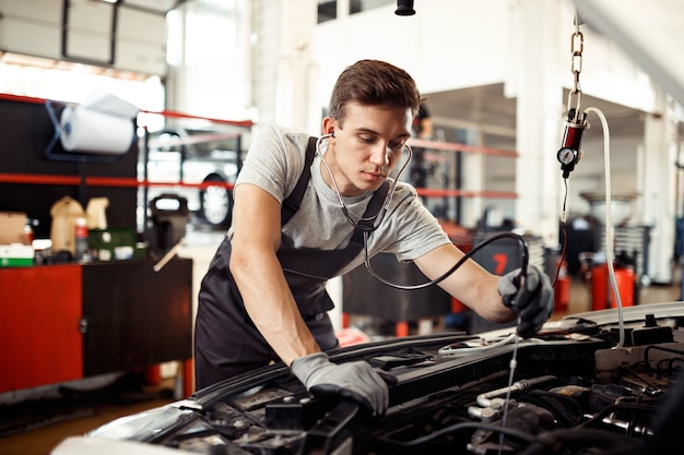 Un giovane è impegnato nel controllo di un motore di un'automobile: riparazione e manutenzione dell'auto.