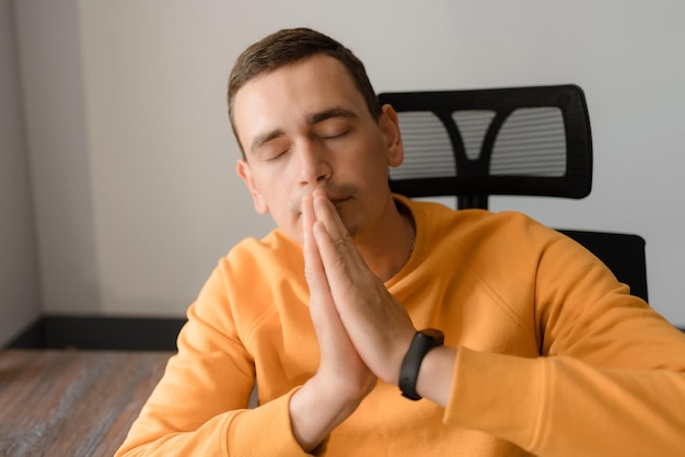Un giovane è seduto a una scrivania e prega con gli occhi chiusi