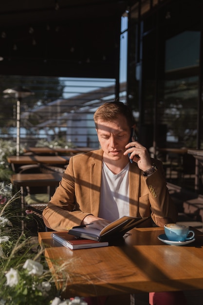 un giovane è seduto in un bar a bere caffè parlando al telefono