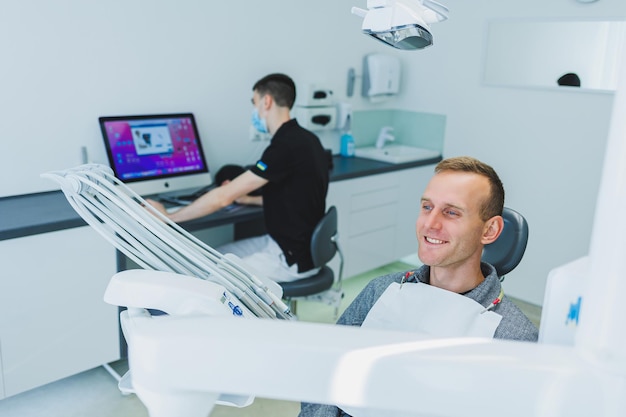 Un giovane è seduto su una poltrona del dentista e un dentista sta lavorando al computer Appuntamento dal dentista