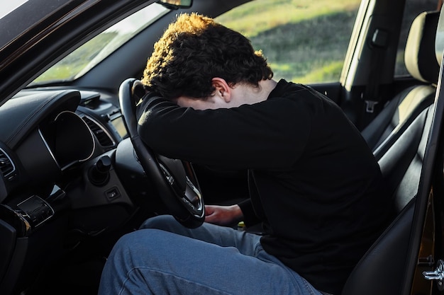 un giovane è stanco per strada e dorme sul volante di un'auto