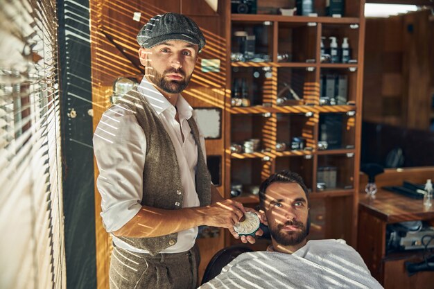 un giovane e un barbiere alla moda che tengono un pennello da barba guardando la telecamera