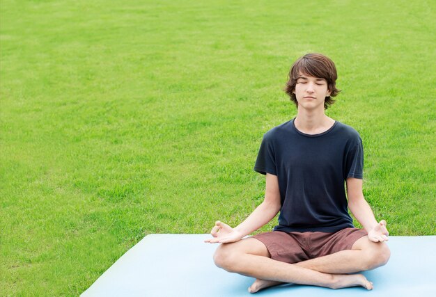 Un giovane fa yoga all'aperto sull'erba verde