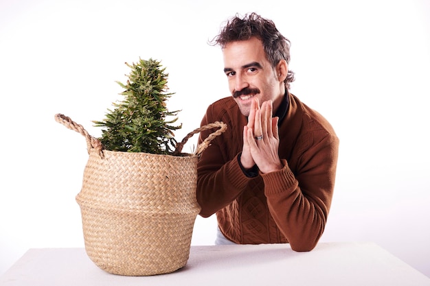 Un giovane felice accanto a una pianta di cannabis con sfondo bianco