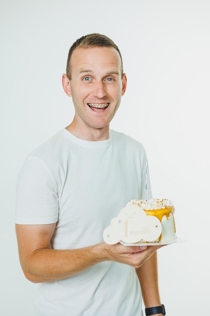 Un giovane felice tiene in mano una torta dolce mentre si trova su uno sfondo bianco