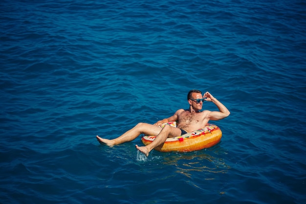 Un giovane galleggia su un cerchio di aria gonfiabile nel mare con acqua blu Vacanza festiva in una felice giornata di sole