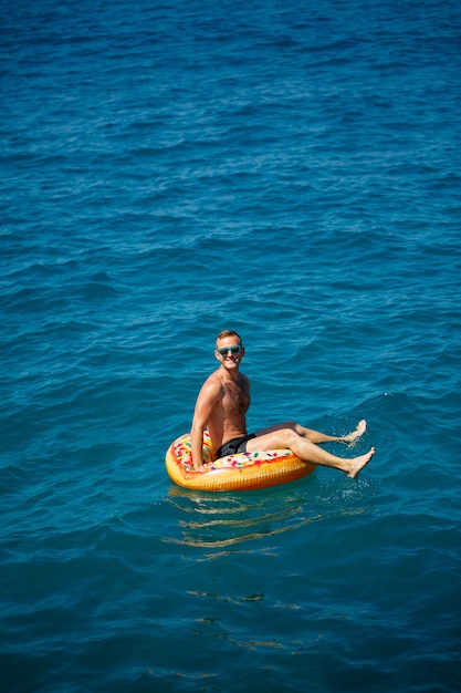 Un giovane galleggia su un cerchio gonfiabile dell'anello d'aria nel mare con acqua blu. Vacanza festiva in una felice giornata di sole. Concetto di vacanza, vista dall'alto.