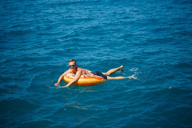 Un giovane galleggia su un cerchio gonfiabile dell'anello d'aria nel mare con acqua blu. Vacanza festiva in una felice giornata di sole.