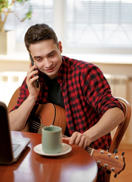 Un giovane impara a suonare la chitarra usando Internet, laptop, lezione online