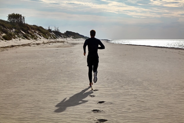 Un giovane in abbigliamento sportivo nero e scarpe da ginnastica arancioni sta facendo jogging sulla spiaggia. Prevenzione dell'ipertensione e delle malattie cardiovascolari