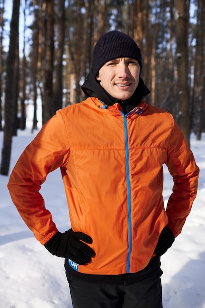 Un giovane in abiti sportivi luminosi si diverte a correre attraverso la foresta in una giornata invernale