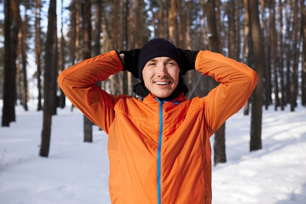 Un giovane in abiti sportivi luminosi si diverte a correre attraverso la foresta in una giornata invernale