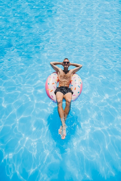 Un giovane in occhiali da sole e pantaloncini si sta rilassando su una ciambella gonfiabile in piscina Vacanze estive