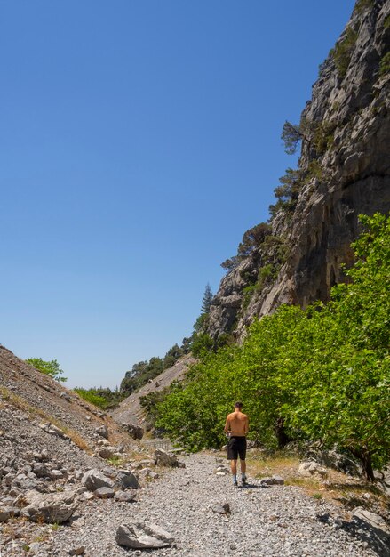 Un giovane in pantaloncini corti e un berretto da baseball cammina attraverso una gola di montagna in Grecia