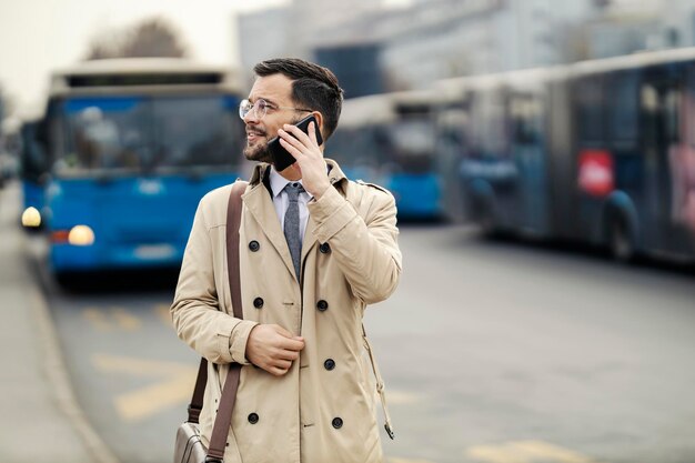 Un giovane in smart casual sta parlando al telefono mentre aspetta un autobus pubblico in una stazione