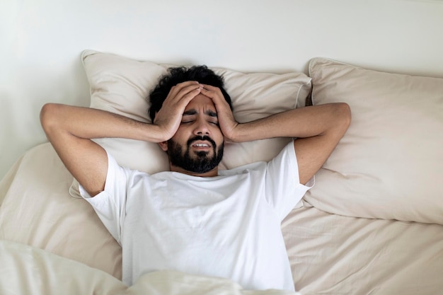Un giovane indiano con emicrania cronica che soffre di mal di testa mentre giace a letto.