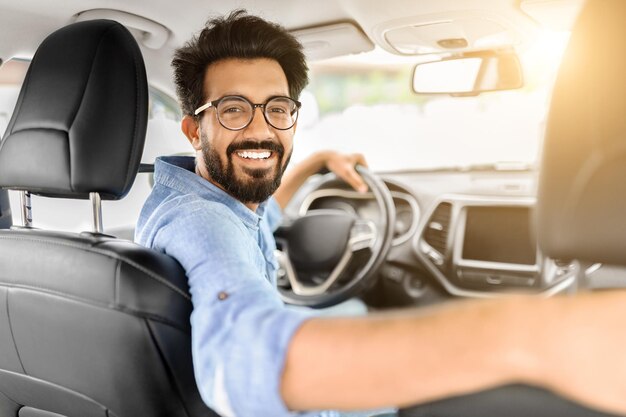 Un giovane indiano felice che impara a guidare seduto in auto