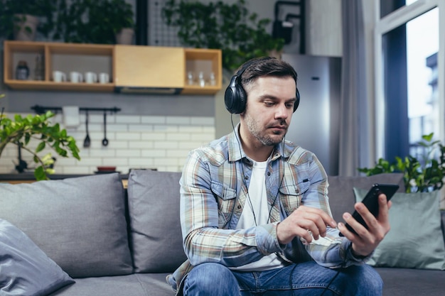 Un giovane lavora da casa con un telefono e le cuffie Parla in videochiamata ascolta musica Seduto sul divano