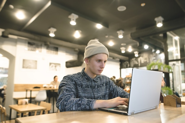 Un giovane libero professionista lavora per un laptop in un accogliente caffè. Lo studente utilizzerà Internet nel bar.