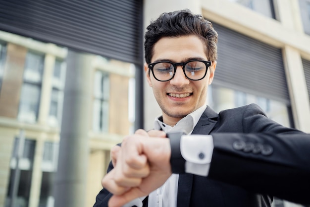 Un giovane manager con gli occhiali sta guardando l'ora in cui un uomo sta digitando un messaggio su uno smartwatch in movimento