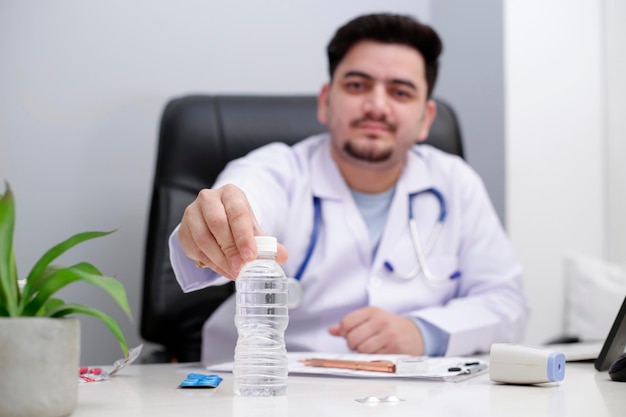 Un giovane medico è seduto sulla sedia della clinica e tiene in mano una bottiglia d'acqua