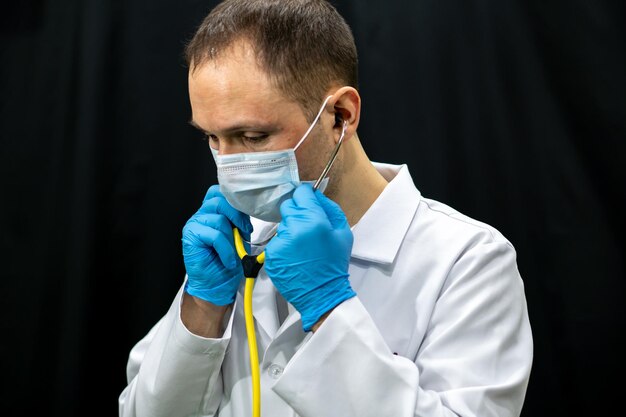 Un giovane medico in guanti blu e uno stetoscopio al collo su sfondo nero Ritratto di un medico con strumenti medici